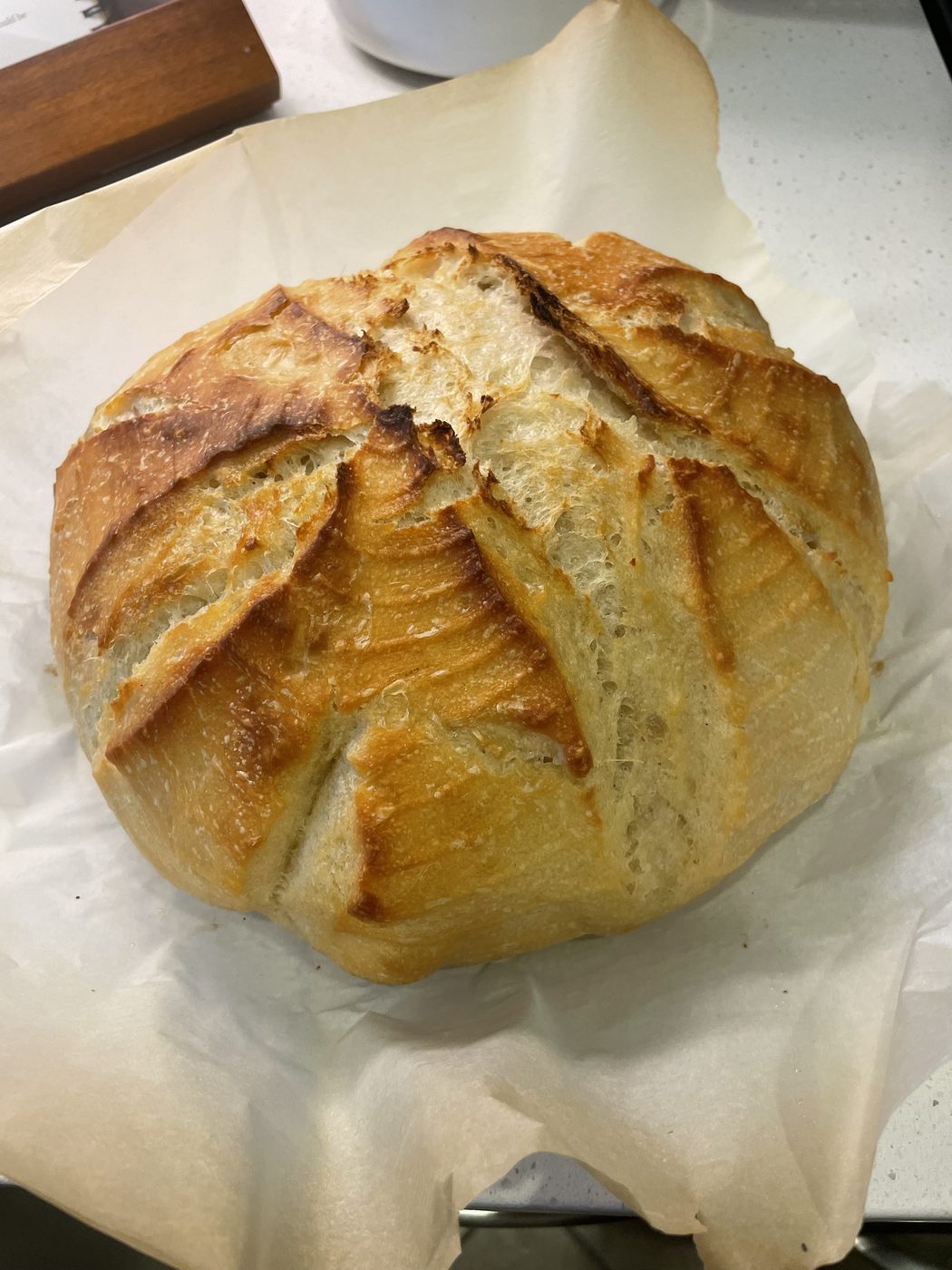 A round sourdough boule with a deep golden crust and a dramatic scored ear across the top, resting on parchment paper.